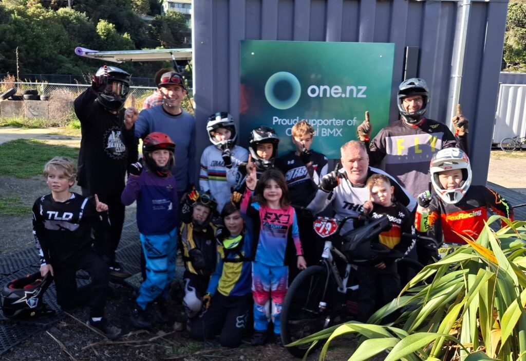 Capital BMX riders gathered round the One NZ sponsor sign on the admin container